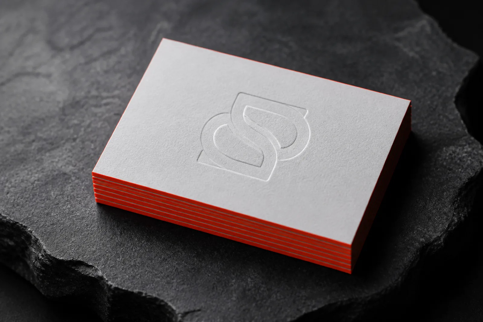 Embossed logo monogram on a stack of cotton business cards with a red accent card